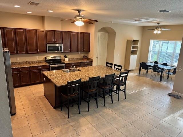 kitchen with a sink, a kitchen bar, arched walkways, a ceiling fan, and appliances with stainless steel finishes