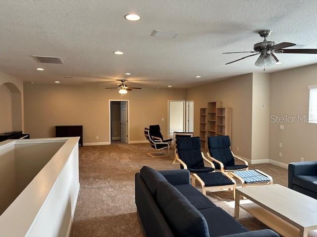 living room with a textured ceiling, carpet, baseboards, visible vents, and ceiling fan