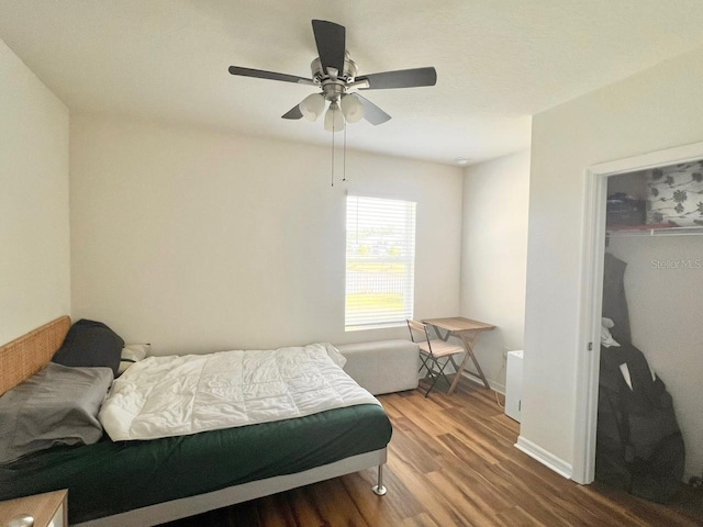 bedroom with wood finished floors, a walk in closet, ceiling fan, a closet, and baseboards