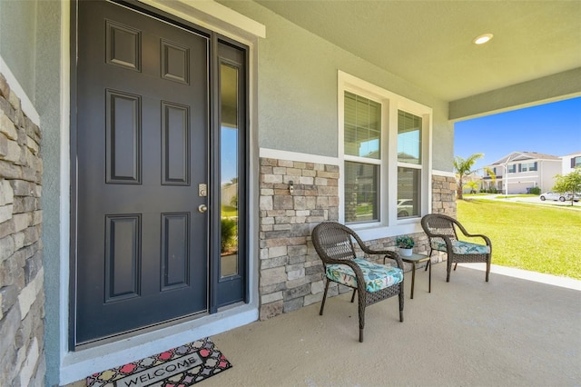 view of exterior entry with a porch, a lawn, stucco siding, and stone siding