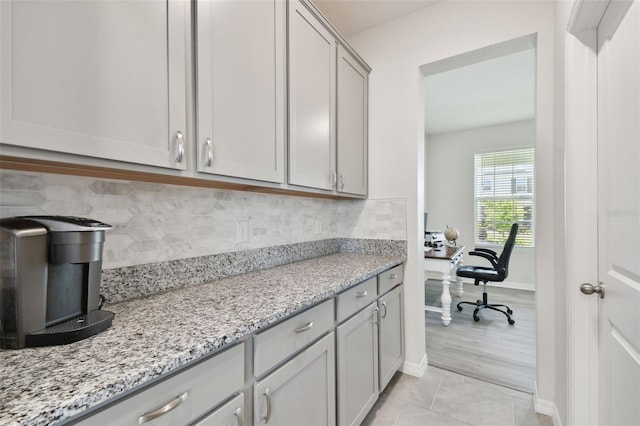 interior space featuring backsplash, light tile patterned floors, gray cabinetry, and light stone countertops