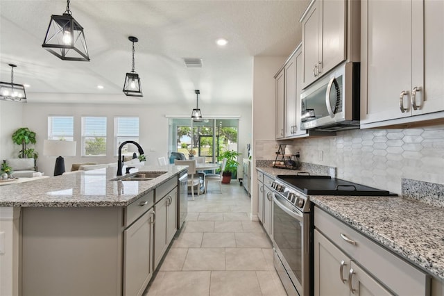 kitchen with a center island with sink, gray cabinets, a sink, backsplash, and stainless steel appliances