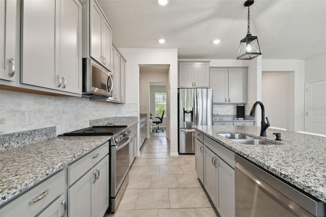 kitchen with hanging light fixtures, appliances with stainless steel finishes, a sink, gray cabinets, and backsplash