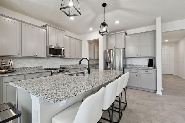 kitchen with a breakfast bar, tasteful backsplash, a sink, appliances with stainless steel finishes, and gray cabinetry