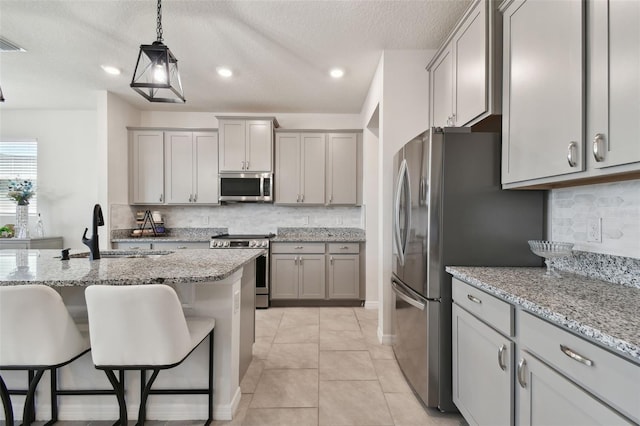 kitchen featuring a sink, appliances with stainless steel finishes, gray cabinets, and a kitchen breakfast bar