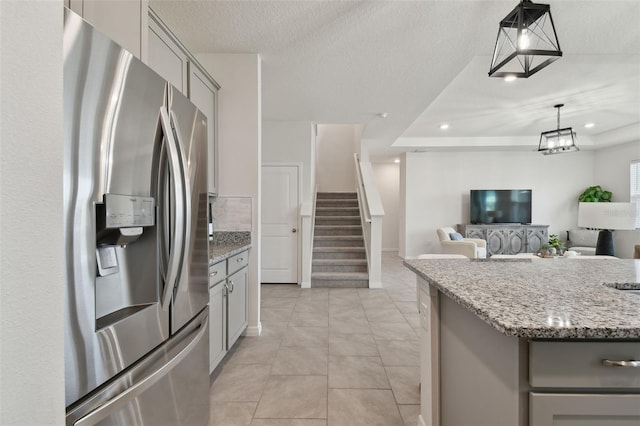 kitchen with gray cabinets, decorative light fixtures, light stone counters, a raised ceiling, and stainless steel fridge