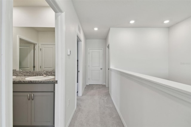 corridor featuring visible vents, baseboards, light colored carpet, recessed lighting, and a sink