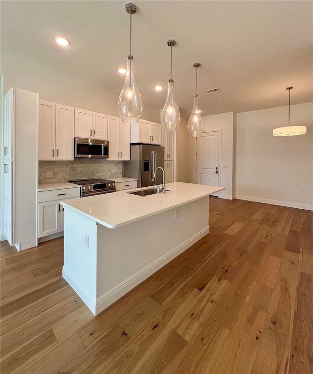 kitchen with decorative backsplash, wood finished floors, white cabinets, a sink, and stainless steel appliances