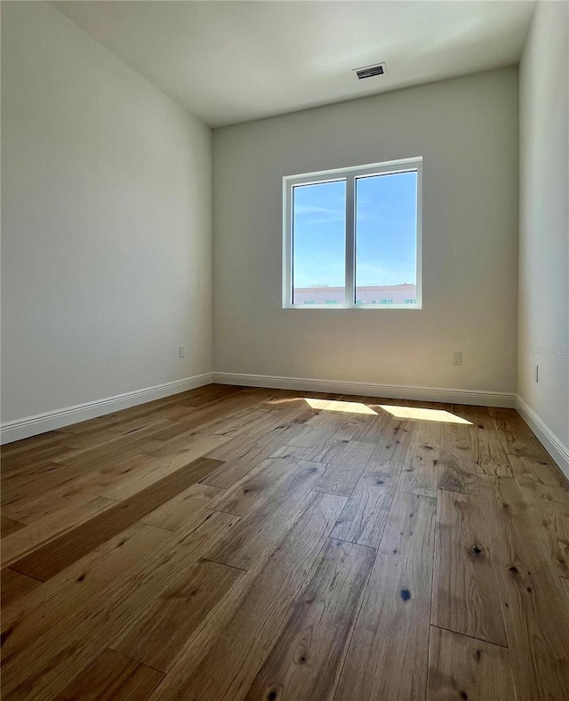 empty room featuring visible vents, baseboards, and wood finished floors