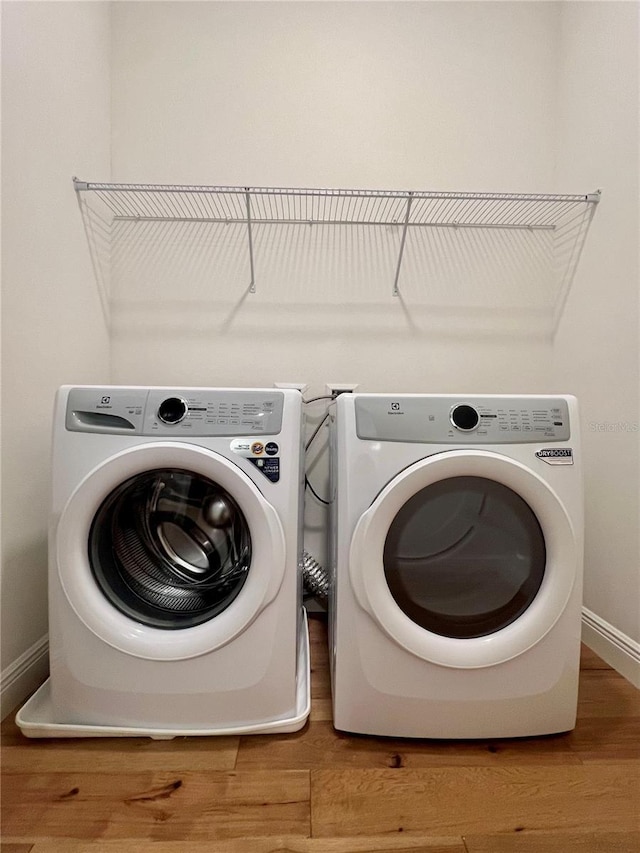 laundry area with baseboards, laundry area, wood finished floors, and washing machine and clothes dryer