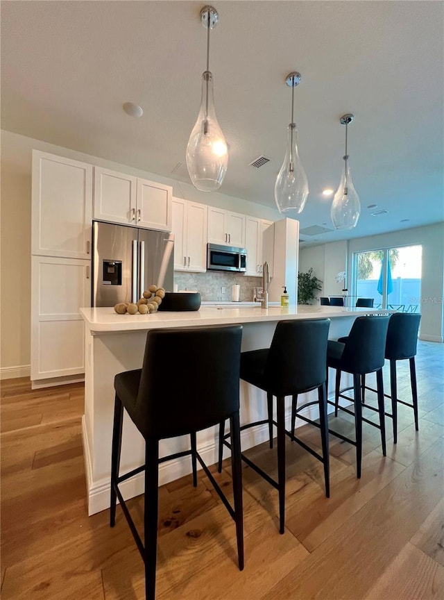kitchen with a large island, visible vents, appliances with stainless steel finishes, tasteful backsplash, and light wood-style flooring