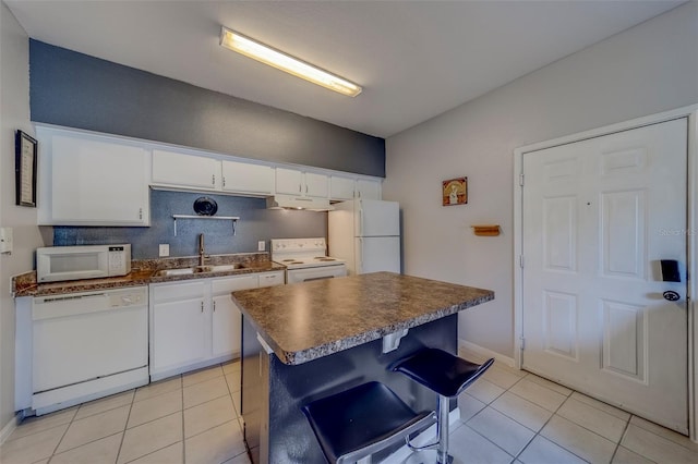 kitchen featuring white cabinets, a sink, dark countertops, white appliances, and light tile patterned floors