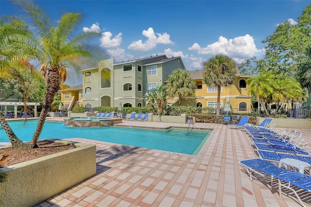 community pool with a patio area, a hot tub, and fence