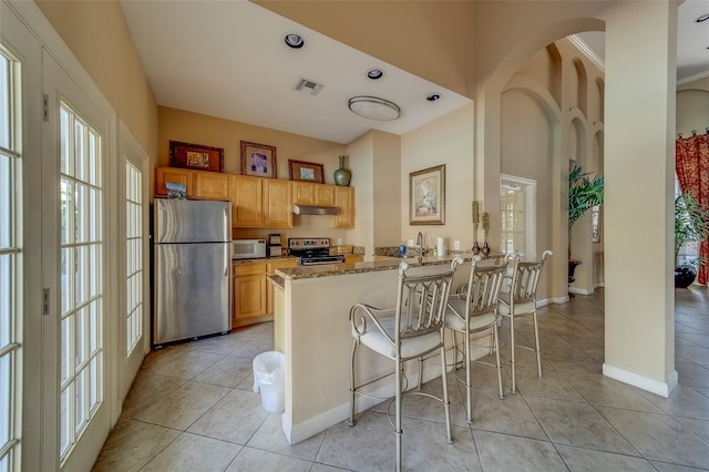 kitchen featuring visible vents, light tile patterned flooring, a peninsula, appliances with stainless steel finishes, and a breakfast bar area