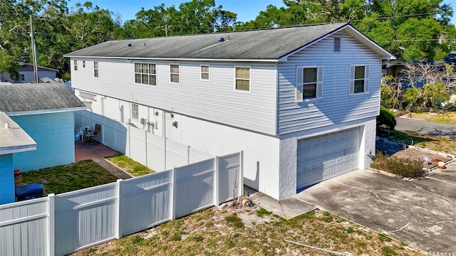 rear view of house featuring fence, concrete driveway, roof with shingles, and a garage