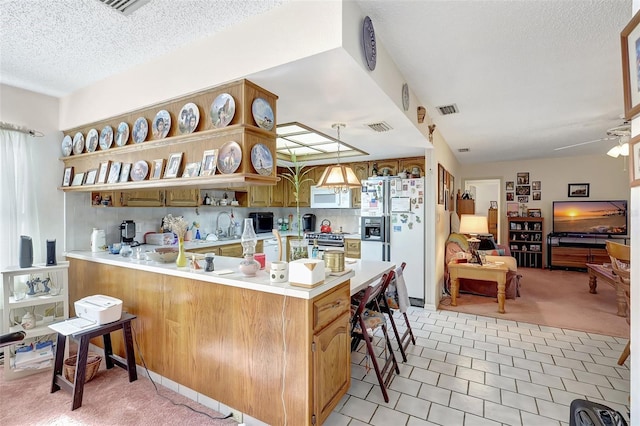 kitchen with a peninsula, a kitchen breakfast bar, visible vents, white appliances, and light countertops