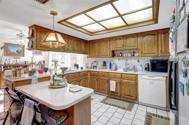 kitchen featuring white dishwasher, light countertops, brown cabinetry, and a sink