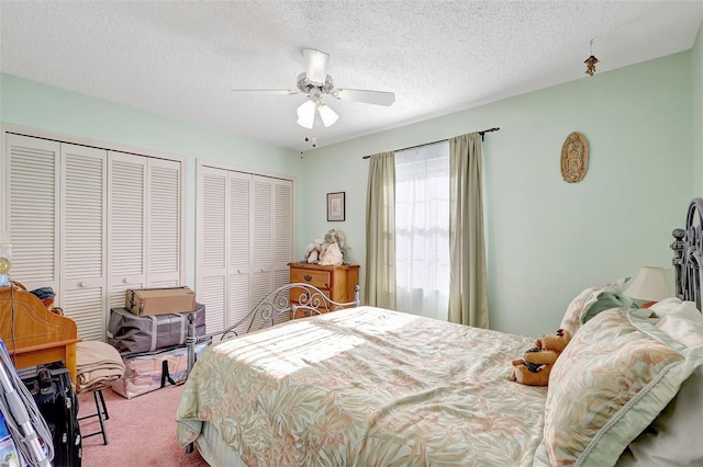 carpeted bedroom with two closets, a textured ceiling, and ceiling fan