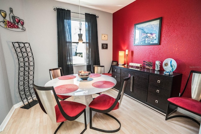 dining room featuring light wood-style flooring, baseboards, and an accent wall