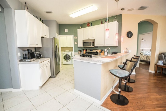 kitchen featuring stainless steel appliances, a peninsula, arched walkways, visible vents, and a breakfast bar area