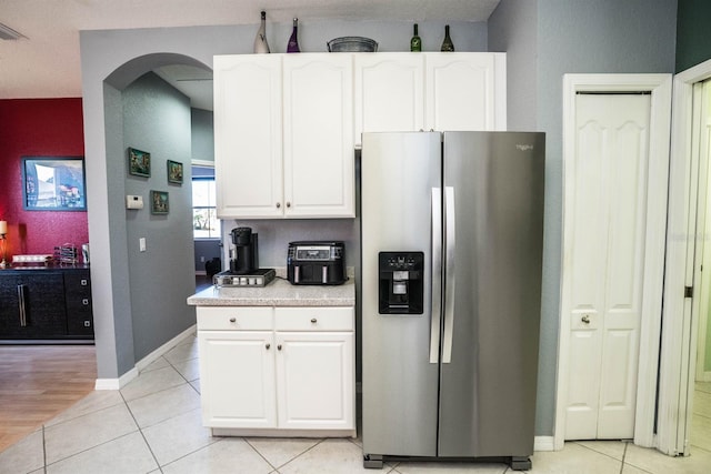 kitchen featuring arched walkways, stainless steel fridge, light countertops, and white cabinetry