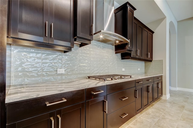 4975 Night Star Trl, Odessa, FL 33556 - kitchen with wall chimney range hood, stainless steel gas cooktop, light stone countertops, dark brown cabinetry, and backsplash