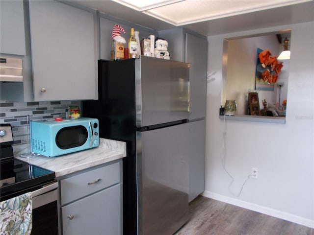 kitchen with tasteful backsplash, wood finished floors, gray cabinets, wall chimney exhaust hood, and appliances with stainless steel finishes