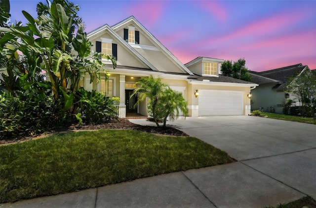 view of front facade with covered porch, driveway, stucco siding, an attached garage, and a yard