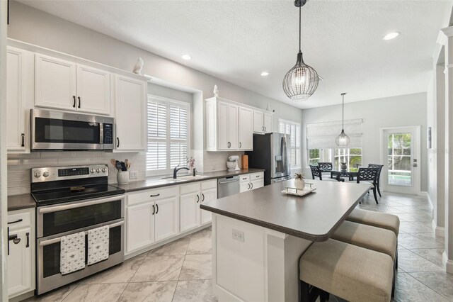 kitchen with a sink, dark countertops, a kitchen island, and stainless steel appliances