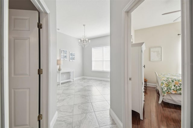 hallway featuring baseboards, a notable chandelier, and marble finish floor