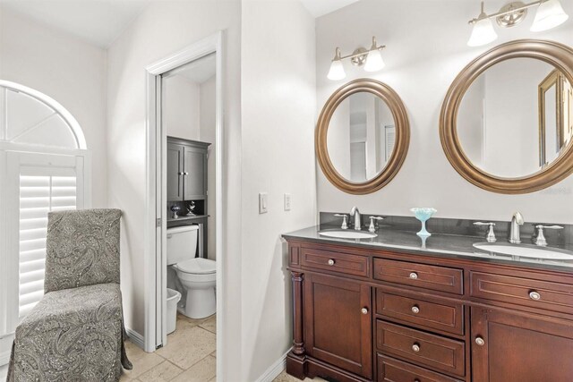 full bathroom featuring baseboards, a sink, double vanity, and toilet