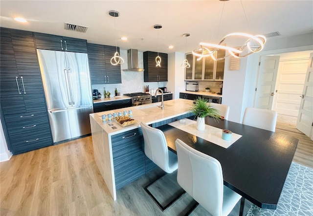 kitchen with a sink, wall chimney range hood, light wood-type flooring, visible vents, and high end appliances
