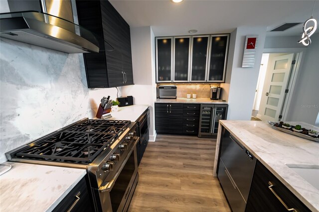 kitchen featuring dark cabinets, stainless steel appliances, wall chimney exhaust hood, and beverage cooler