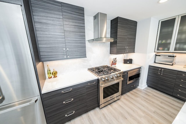 kitchen with light wood-style flooring, modern cabinets, wall chimney exhaust hood, light countertops, and appliances with stainless steel finishes