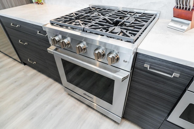 details featuring dark cabinetry, light countertops, stainless steel range, and light wood-style floors