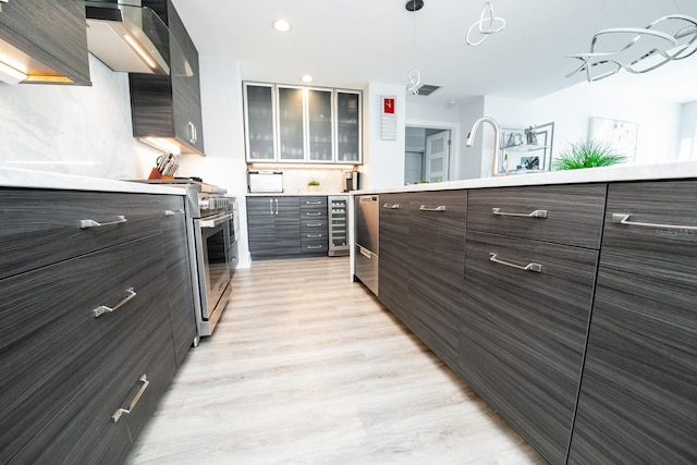kitchen with wall chimney exhaust hood, dark brown cabinetry, light wood-style flooring, light countertops, and glass insert cabinets