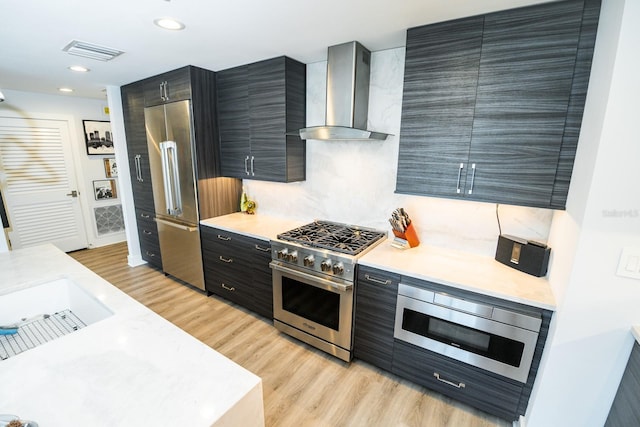 kitchen featuring light wood-style flooring, visible vents, high quality appliances, wall chimney range hood, and light countertops