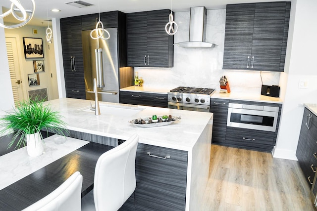 kitchen featuring light countertops, wall chimney exhaust hood, high quality appliances, and light wood-style flooring
