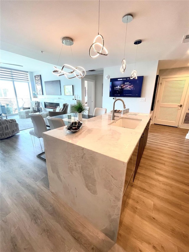 kitchen with light wood-style floors, light stone counters, an island with sink, and a sink