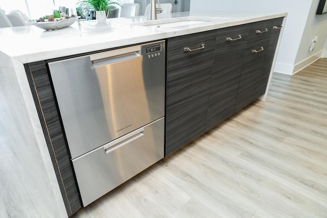 kitchen featuring stainless steel dishwasher, light wood finished floors, a sink, and modern cabinets
