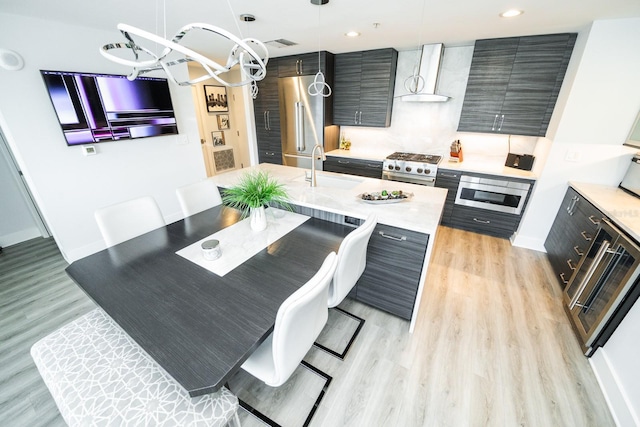 kitchen with light countertops, a sink, high end appliances, modern cabinets, and wall chimney range hood