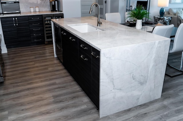 kitchen with a sink, a center island with sink, dark wood-style floors, beverage cooler, and dark cabinetry