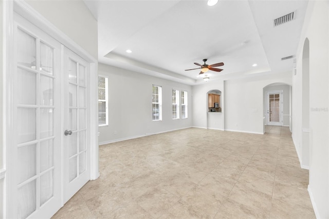 unfurnished living room with ceiling fan, a raised ceiling, arched walkways, french doors, and visible vents