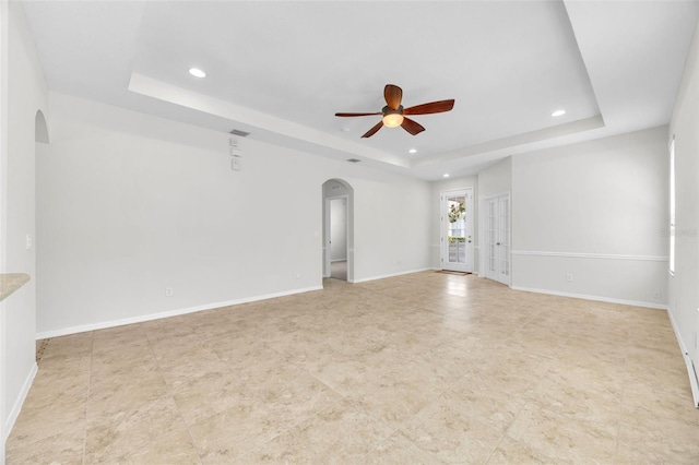 tiled empty room with a ceiling fan, arched walkways, baseboards, a tray ceiling, and recessed lighting