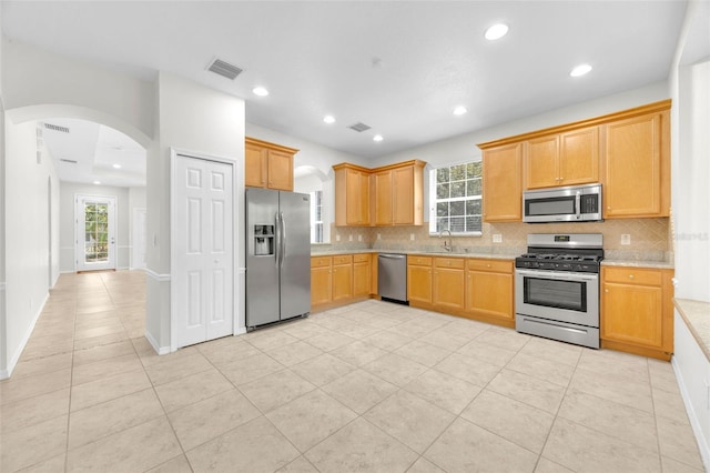 kitchen with decorative backsplash, appliances with stainless steel finishes, arched walkways, a sink, and light countertops