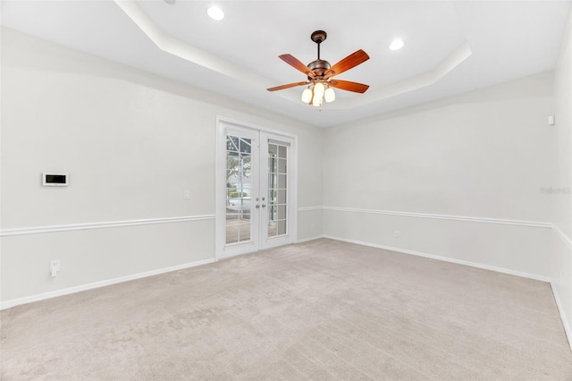 unfurnished room featuring ceiling fan, french doors, light colored carpet, a raised ceiling, and baseboards