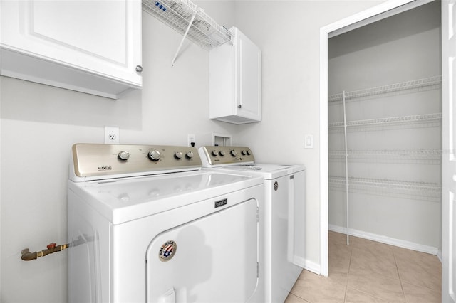 laundry room featuring separate washer and dryer, baseboards, cabinet space, and light tile patterned floors