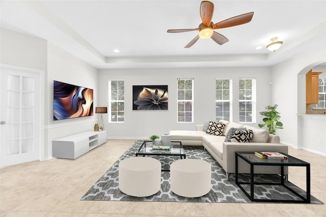 living room with a ceiling fan, baseboards, a raised ceiling, tile patterned floors, and arched walkways