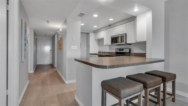 13720 Gulf Blvd Unit 305, Madeira Beach, FL 33708 - kitchen featuring a breakfast bar area, visible vents, stainless steel appliances, light wood finished floors, and a peninsula