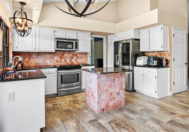 kitchen featuring white cabinets, stainless steel appliances, a sink, dark stone counters, and a chandelier